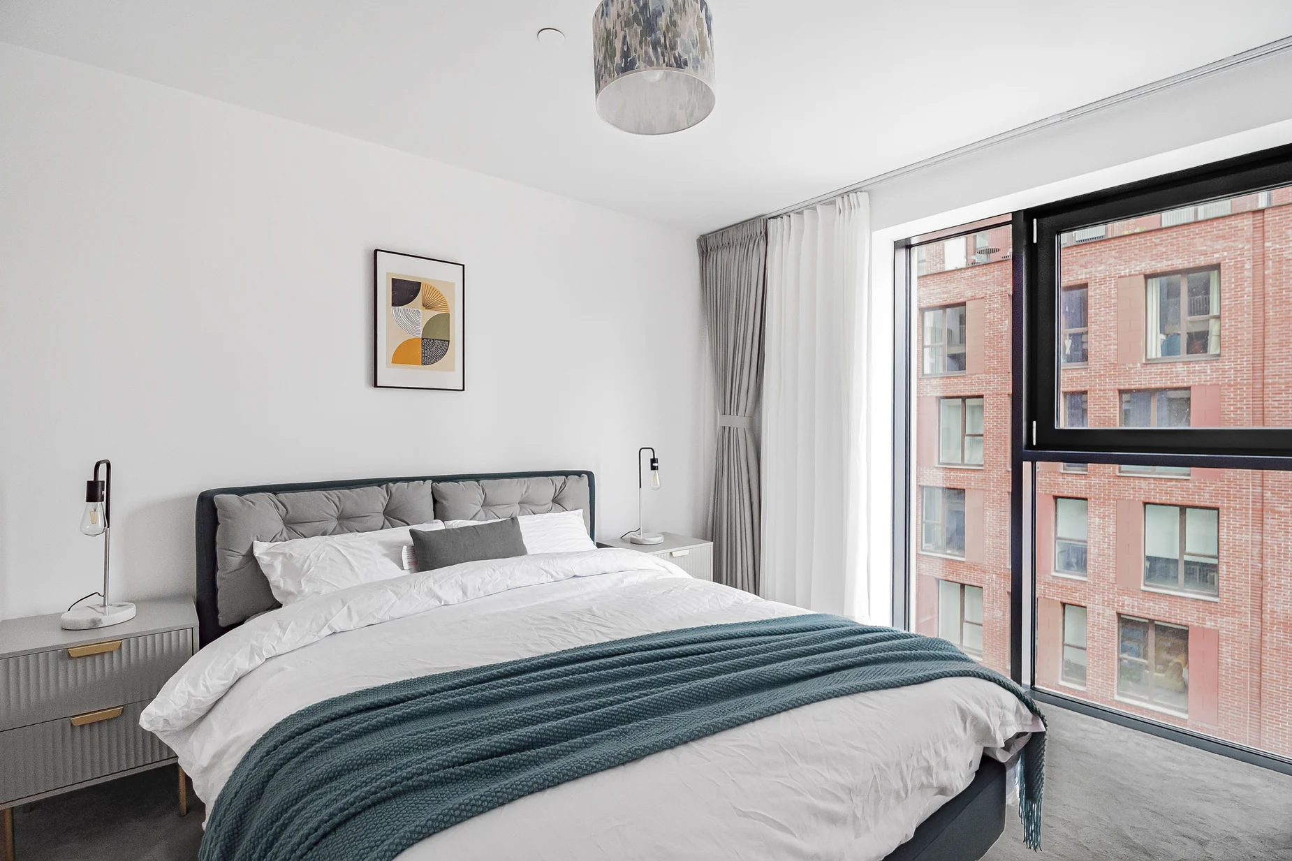 Bright main bedroom with upholstered bed, white bedding and muted blue throw, framed artwork and window dressing