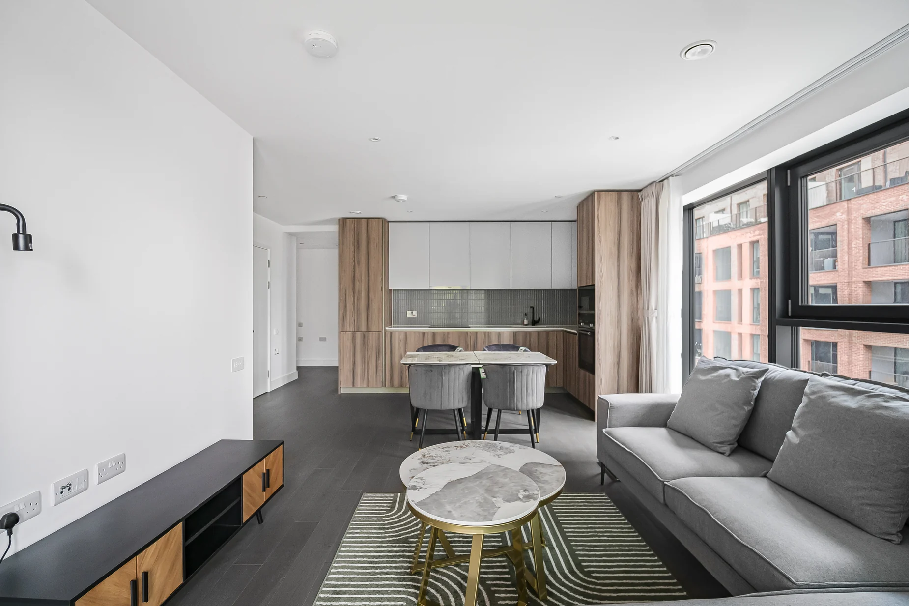 Furnished open-plan living room at Hawksbury Heights, with grey sofa, sideboard, dining table and fitted kitchen