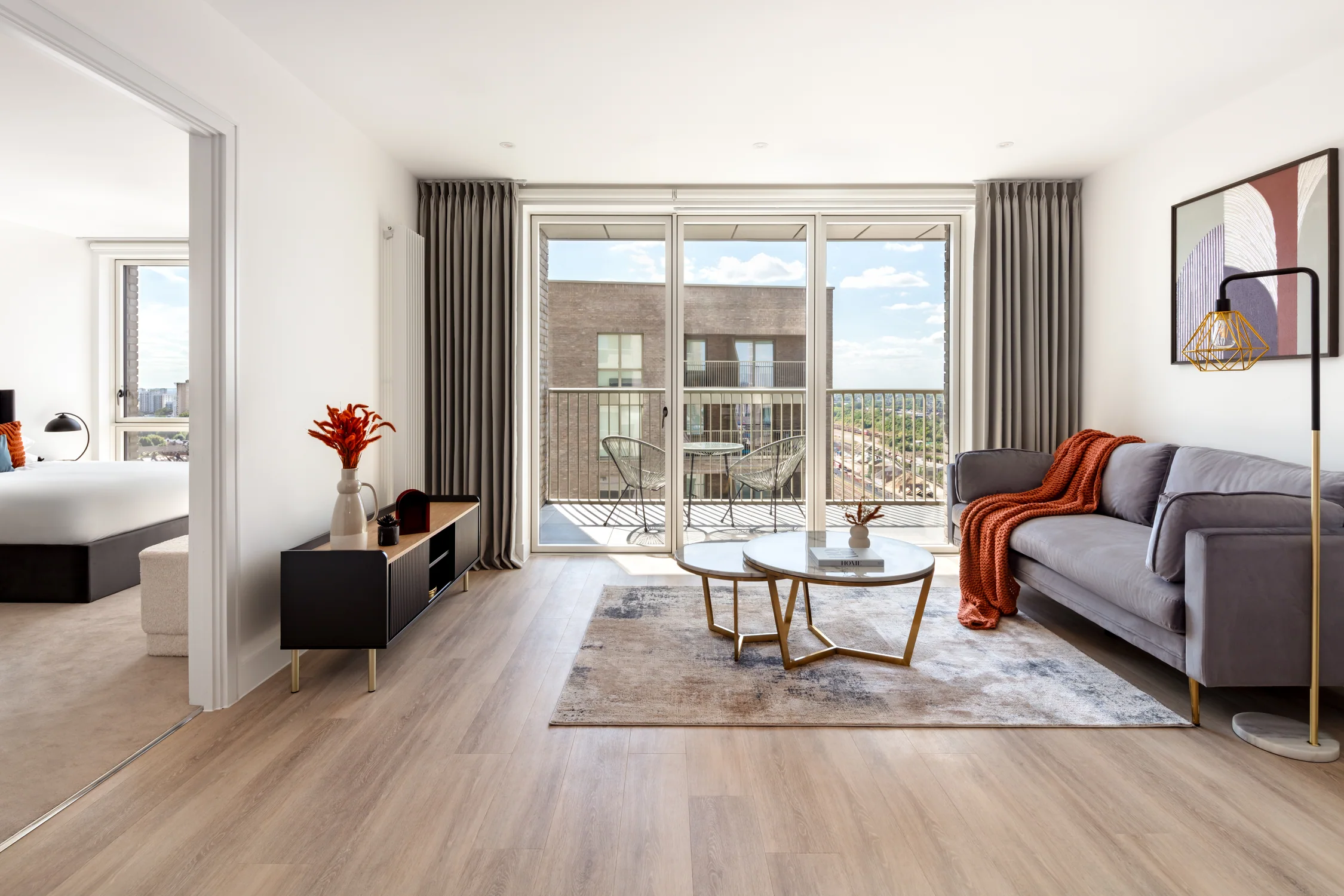 Bright living room with soft grey sofa, orange throw, floor lamp and sliding balcony doors