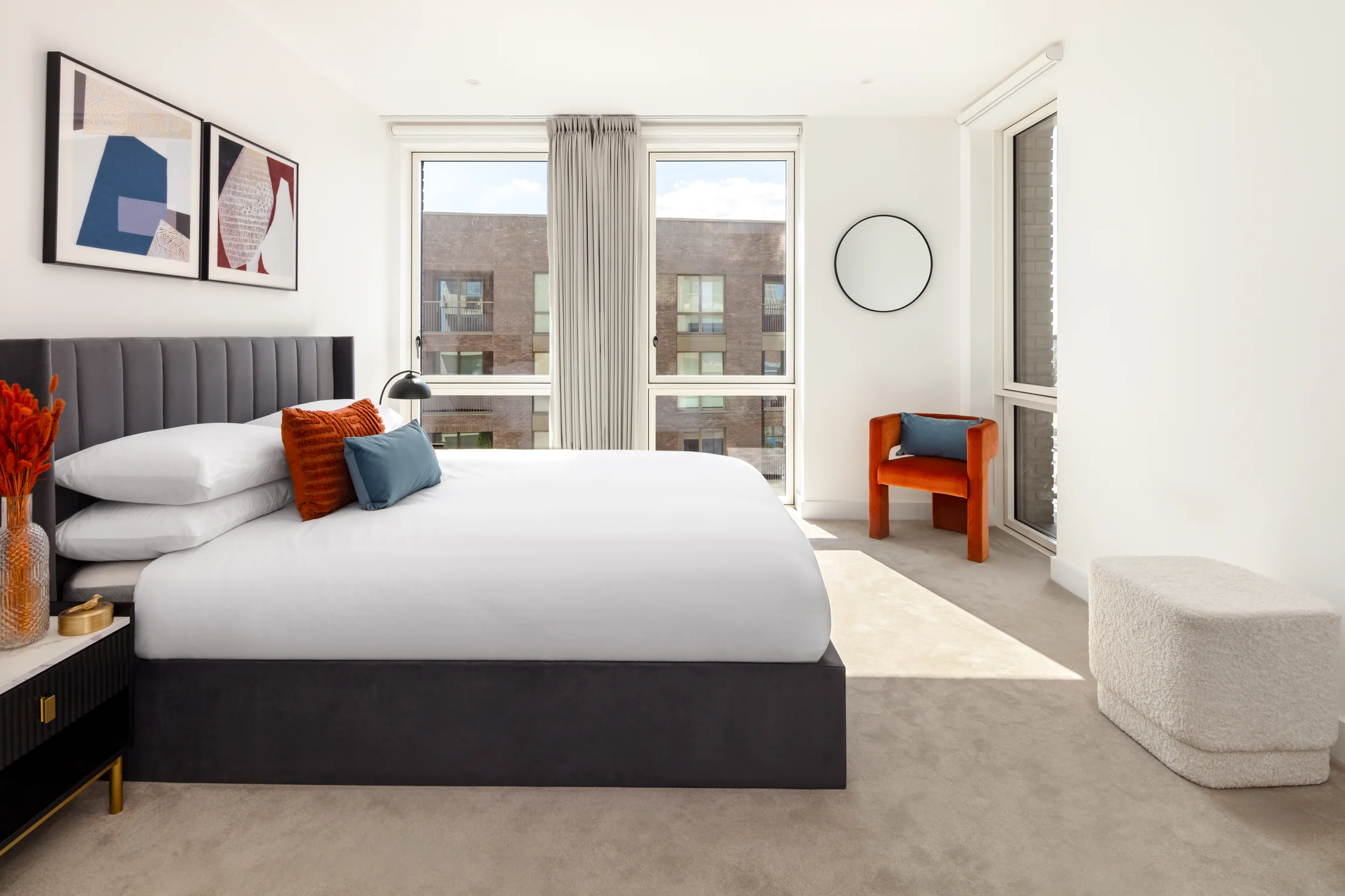 Dressed bedroom with grey upholstered headboard, white bedding and blue and burnt-orange cushions