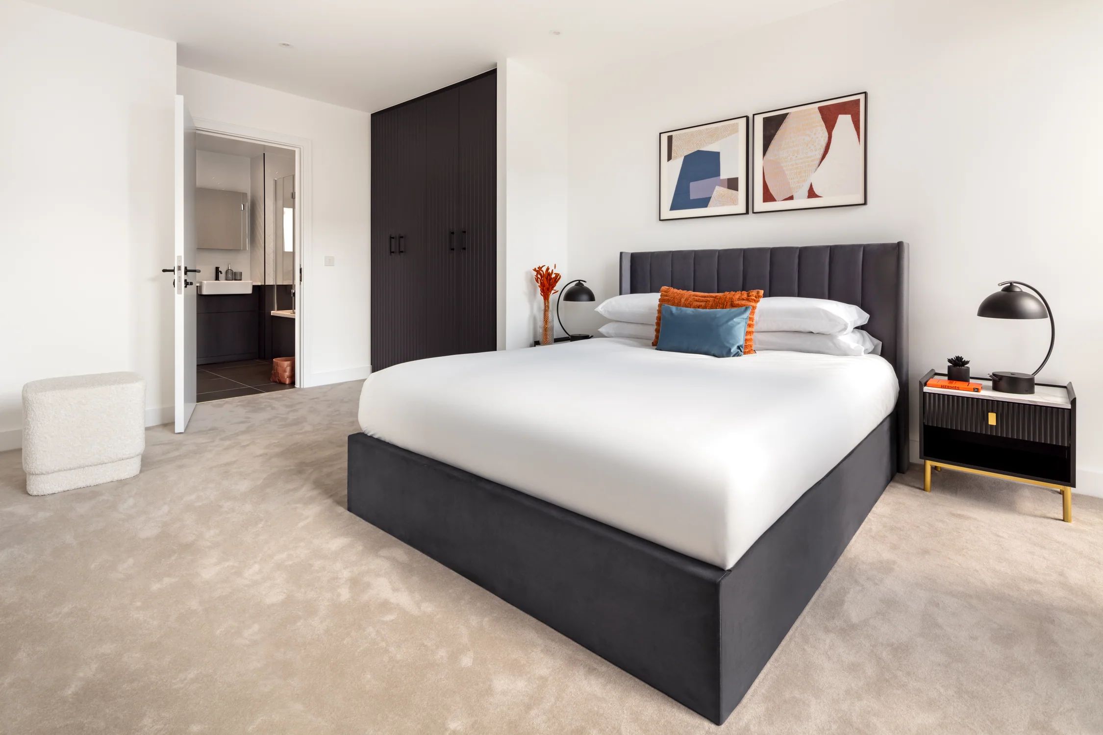 Full view of the furnished one-bedroom apartment bedroom with grey upholstered bed, black wardrobe and colourful artwork
